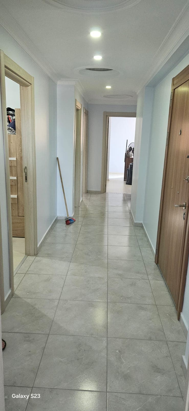 Tamamlanmış koridor boyaması, açık mavi duvarlar, gri fayans zemin, ahşap desenli giriş kapısı