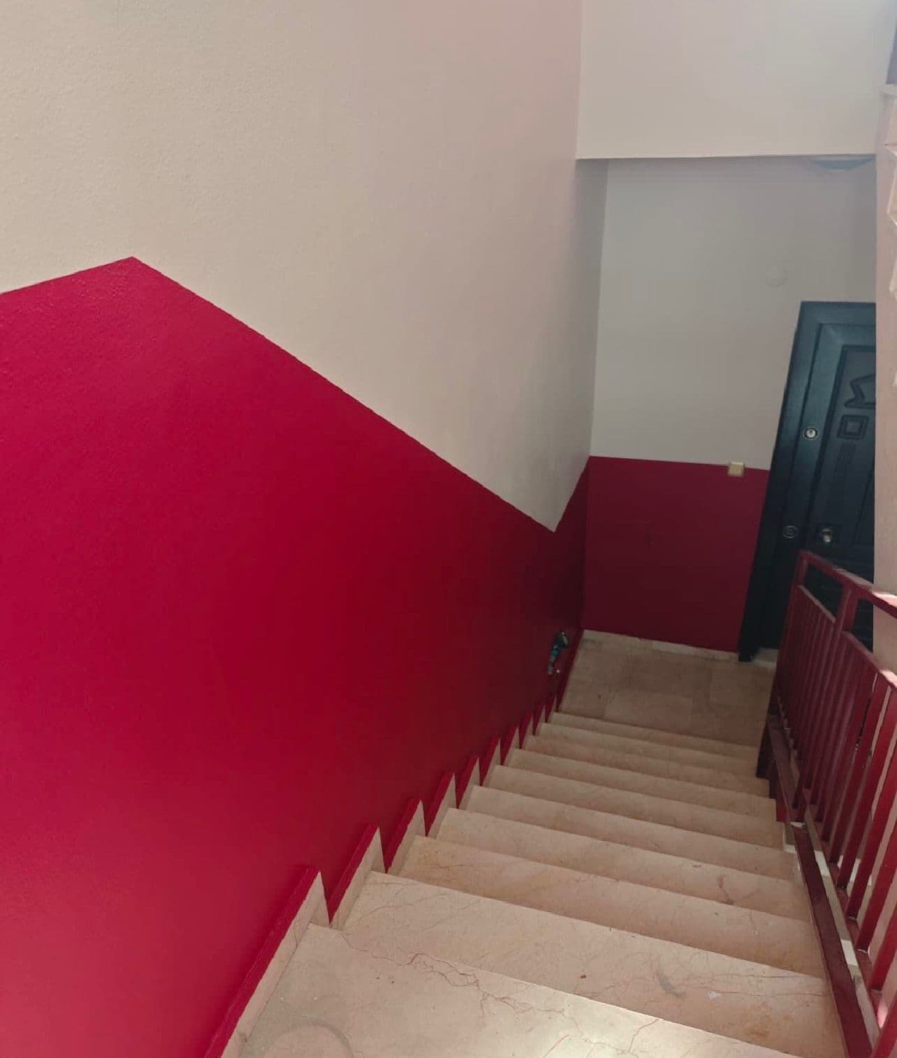 Apartman merdiven boşluğu, kırmızı-beyaz iki renkli açılı duvar boyama, mermer basamaklar