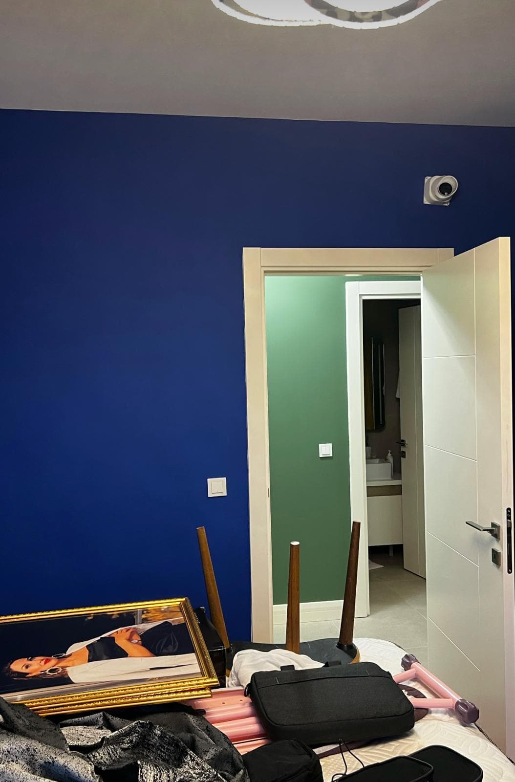 Lacivert boyanmış yatak odası duvarı, açık kapıdan görünen yeşil boyalı banyo girişi