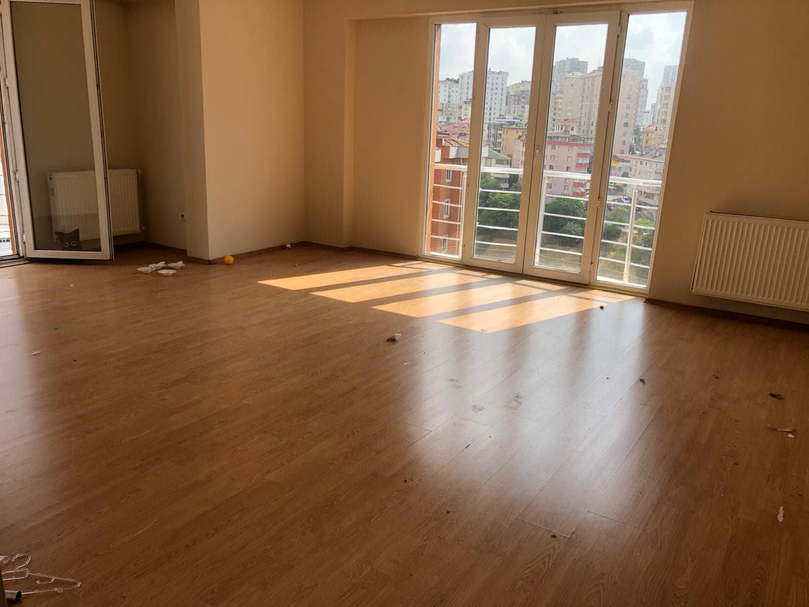 Boş oda, bal rengi/kırmızımsı kahverengi laminat zemin, şehir manzaralı balkon kapısı, radyatör