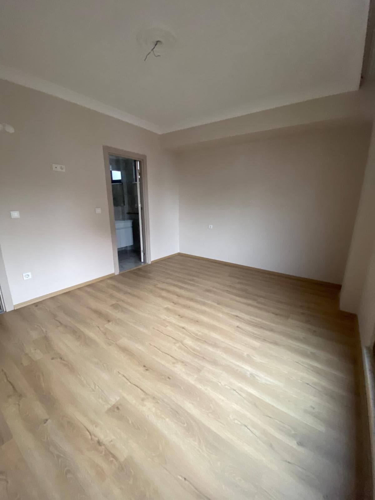 Boş oda, ebeveyn banyosuna açılan kapı görünümü, beyaz lavabo, bej duvar tonları