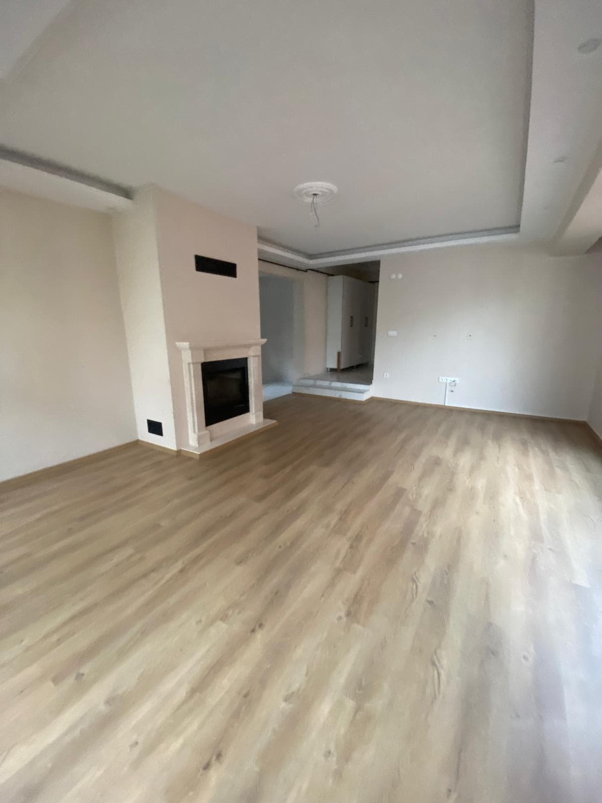 Şömineli salon, krem duvarlar, siyah gömme somineli mermer sova, tepsi tavan, bitişik odaya açılan yükseltilmiş basamak